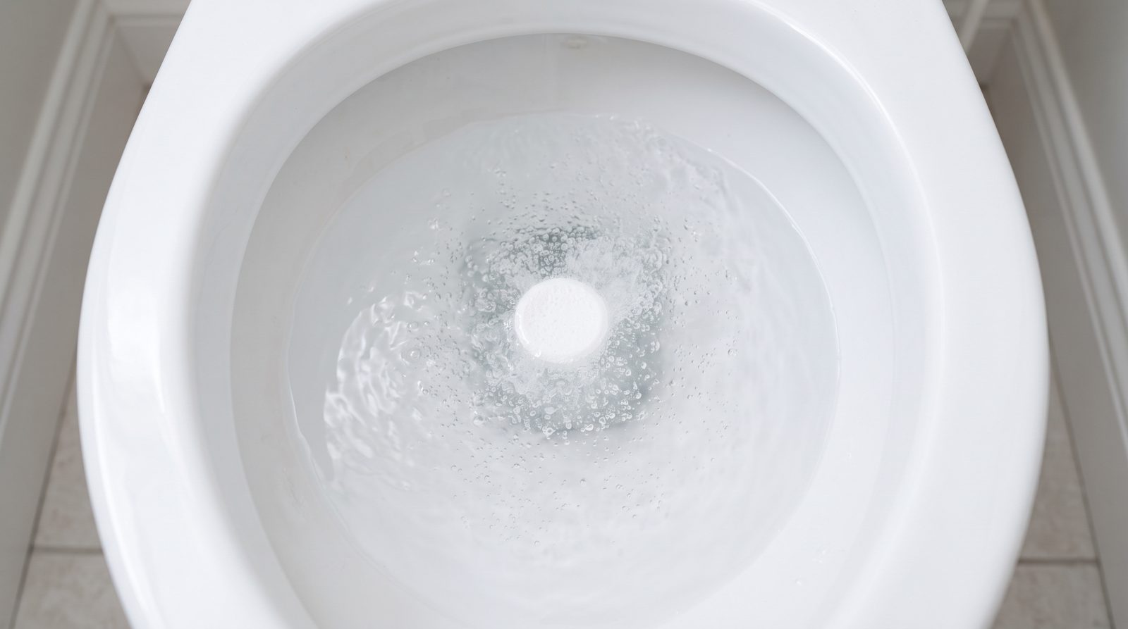 septic tank tablet being placed near a toilet bowl in a home bathroom, neutral household scene